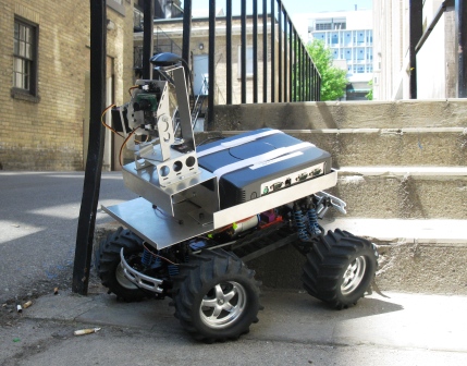 Four-wheeled ART team robot with sensors and cameras, climbing a concrete stair outdoors.